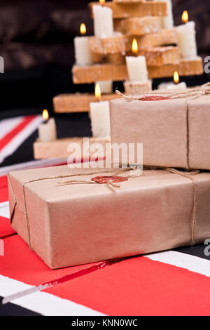 Boxen, eingewickelt in Handwerk Papier, mit packthread mit einem Wafer auf dem Hintergrund eines hölzernen Leuchter auf einem farbigen hölzernen Schreibtisch behoben. Stockfoto