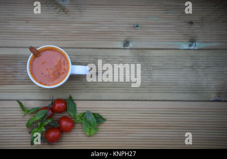 Essen Fotografie Bild der hausgemachten Tomatensuppe in Weiß Tasse oder Becher mit frischen Zutaten von Tomaten und Basilikum Blätter im Hintergrund auf Holz mit Platz Stockfoto