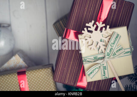 Weihnachten Geschenke in Kartons dfferent Größe. Eine beige Geschenkbox mit Schleife mit Frohe Weihnachten Inschrift gebunden, gemusterte Kartons mit rot metallic Ribbon Stockfoto