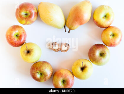 Gruppe von farbigen reife Äpfel und Birnen in Form von Herzen und zwei Hälften von Walnut in Form von Herzen in der Mitte auf weißem Hintergrund. Ansicht von oben. Stockfoto