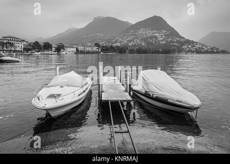 Berge und See in Lugano in der Schweiz. Die Boote sind im Vordergrund. Die Schwarz-Weiß-Fotografie. Stockfoto