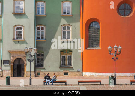 Krakau-Polen-Farbe, ein Paar sitzt in der Nähe der bunten Fassaden der alten Stadtgebäude auf der Westseite des Kleinen Marktplatzes (Maly Rynek) in Krakow. Stockfoto