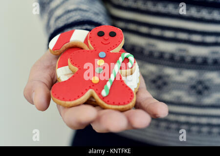 Nahaufnahme eines jungen kaukasischen Mann mit einem Pullover, mit einem Stapel von handgefertigten Weihnachtsplätzchen mit verschiedenen Formen und Farben in der Hand Stockfoto