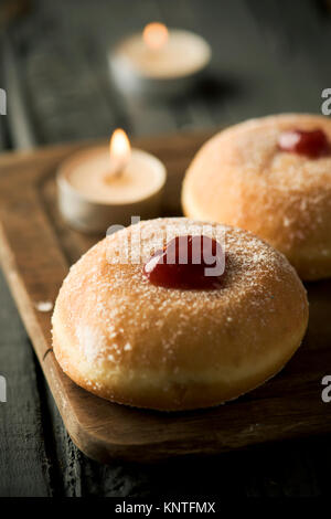 Nahaufnahme von einigen sufganiyot, jüdische Krapfen gefüllt mit Strawberry jelly traditionell gegessen auf Hanukkah, und einige Kerzen, auf einem rustikalen Holztisch Stockfoto