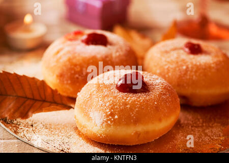 Nahaufnahme von einigen sufganiyot, jüdische Krapfen gefüllt mit Strawberry jelly traditionell gegessen auf Hanukkah, und einige Kerzen auf einem Tisch Stockfoto