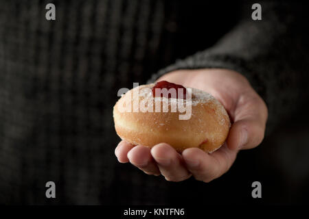 Nahaufnahme eines sufganiyah, eine jüdische Krapfen gefüllt mit Strawberry jelly traditionell gegessen auf Hanukkah, in der Hand eines Mannes Stockfoto