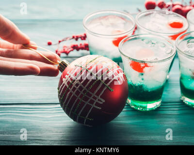 Weihnachten Urlaub Partei grüne Alkohol Getränke mit Kirsche. Urlaub Vorbereitung dekorieren Konzept. Woman's Hand halten roten Weihnachtskugel Stockfoto