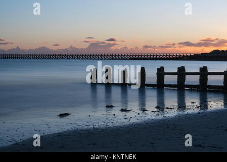 Malerische Landschaft Blick auf See Defense Buhnen mit Reflexionen an Littlehampton, West Sussex, UK bei Sonnenuntergang mit geglätteten lange Belichtung ruhiges Meer Stockfoto