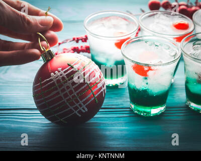 Weihnachten Urlaub Partei grüne Alkohol Getränke mit Kirsche. Urlaub Vorbereitung dekorieren Konzept. Woman's Hand halten roten Weihnachtskugel Stockfoto