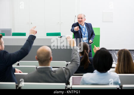 Zuversichtlich älterer Geschäftsmann, Fragen zu Kollegen, während sie eine Präsentation im Vortragssaal Stockfoto