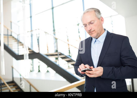 Zuversichtlich älterer Geschäftsmann von SMS-Nachrichten auf dem Smartphone im Büro Stockfoto