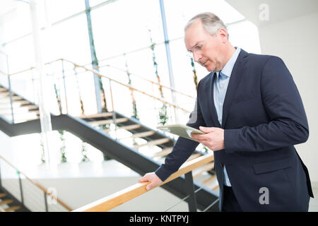 Senior Geschäftsmann mit Tablet Computer während lehnte sich auf Geländer in Office Stockfoto