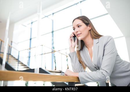 Zuversichtlich Geschäftsfrau mit Smartphone, während lehnte sich auf Geländer in Office Stockfoto