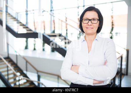Portrait von zuversichtlich reife Geschäftsfrau im Amt stehende Arme gekreuzt Stockfoto