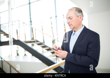 Zuversichtlich älterer Geschäftsmann Messaging auf dem Smartphone im Büro Stockfoto