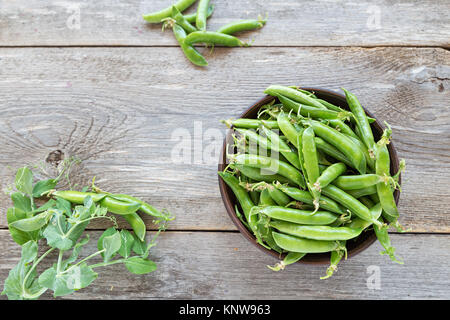 Junge Erbsen in einem Ton Platte auf einen hölzernen Tisch. Neben eine Platte der pea Pods. Neben der Platten ist der Stiel von Erbsen. Stockfoto