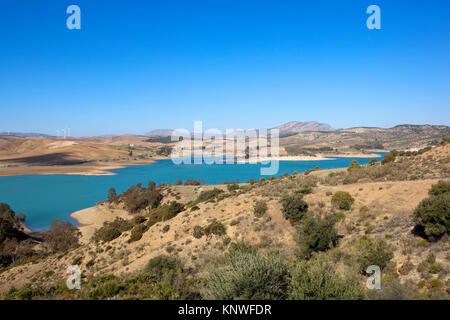 Ein blauer See in sandigen Dürren Berglandschaft mit Bäumen und Windkraftanlagen unter einem blauen Himmel in Andalusien Spanien Stockfoto