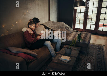 Junges Paar zusammen entspannt auf einem Sofa und einen Laptop verwenden. Der Mann und die Frau mit Laptop in ein gemütliches Wohnzimmer. Stockfoto