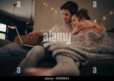 Junges Paar sitzt auf einem Sofa zu Hause im Winter und mit Laptop Computer. Gemütliche Paar in hygge Haus mit Laptop. Stockfoto