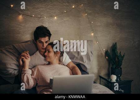 Romantische junge Paar mit Laptop auf dem Bett. Mann und Frau in der Liebe Video auf Laptop beim Entspannen im Schlafzimmer. Stockfoto