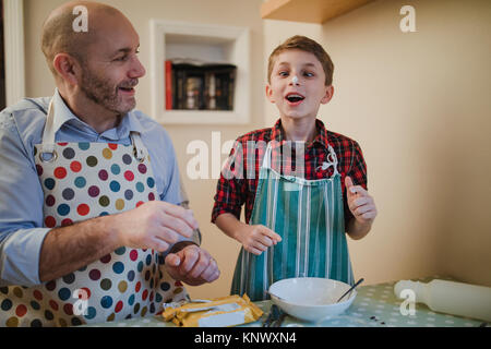 Kleine Junge ist, festliches Gebäck mit seinem Vater zu Weihnachten. Er hat Sahnehäubchen auf seine Nase und kreuzt seine Augen zu sehen ist. Stockfoto