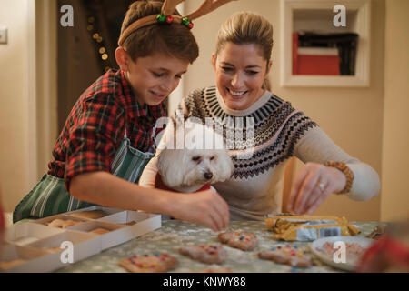Kleine Junge ist Dekoration Weihnachten Kekse zu Hause mit seiner Mutter und ihrem Hund. Stockfoto