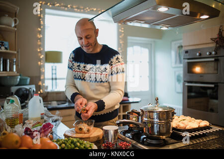 Ein reifer Mann bereitet ein Weihnachtsessen in der Küche seiner Wohnung. Er ist Schälen von Karotten und Pastinaken. Stockfoto