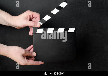 Eine leere Klappe offen gehalten, als ob ungefähr zu reißen, die zwischen den Händen eines männlichen operativen mit schwarzen Schiefertafel Hintergrund schliessen. Stockfoto