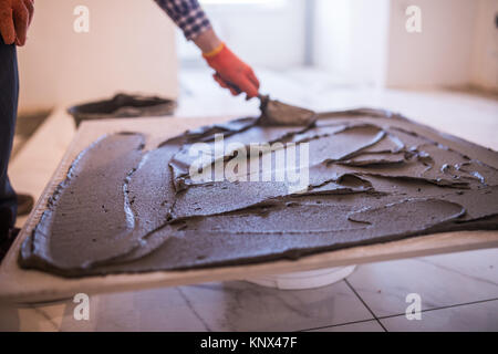 Festlegung von Keramikfliesen. Troweling Mörtel auf Betonboden in der Vorbereitung für die Verlegung von Bodenfliesen. Stockfoto