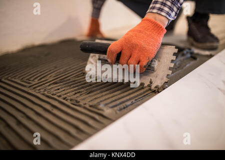 Troweling Mörtel auf Betonboden in der Vorbereitung für die Verlegung von weißen Bodenfliesen. Stockfoto