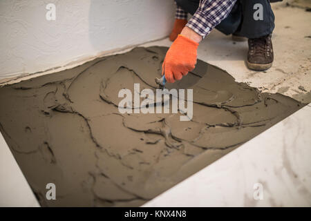 Festlegung von Keramikfliesen. Troweling Mörtel auf Betonboden in der Vorbereitung für die Verlegung von Bodenfliesen. Stockfoto