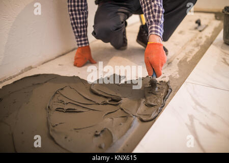 Troweling Mörtel auf Betonboden in der Vorbereitung für die Verlegung von weißen Bodenfliesen. Stockfoto