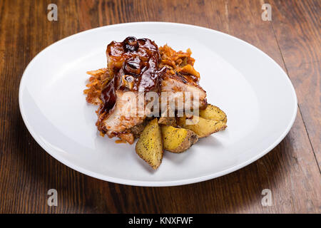 Auf dem Tisch ist eine Platte von gegrillten Rippchen, Sauerkraut, gebackene Kartoffeln und Salat letuk Stockfoto