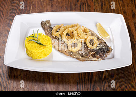 Auf dem Tisch eine Platte mit gegrilltem Fisch Forelle mit Zitrone, gebratene Zwiebelringe, mit Sesam und als Beilage Reis und Rosmarin. Stockfoto