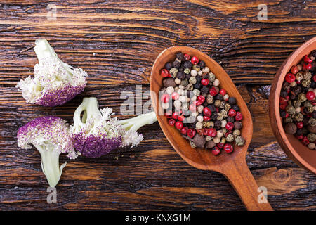 Bunte Paprika Erbsen in einem Löffel und einer Platte auf einem braunen Holztisch Stockfoto