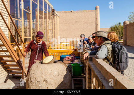 Eine lokale Frau backt Brot in einem traditionellen Lehmofen beobachtete eine Gruppe von Touristen, Chiwa, Usbekistan Stockfoto