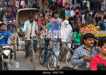 Eine Rikscha Radfahrer und zwei muslimischen Frauen Fahrräder durch eine geschäftige und überlasteten Dasashwamedha Ghat Straße in Varanasi, Indien drücken Stockfoto