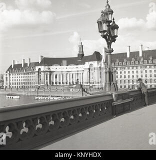 1950, historische, Mann stehend auf die Westminster Bridge, London und die Themse und mit der eindrucksvollen County Hall Building, das ehemalige Hauptquartier der Greater London Council (GLC) auf seiner Rechten, an der South Bank. Stockfoto