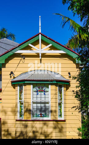 Erkerfenster auf Gelb traditionelle australische Queenslander House mit Blechdach und tropischen Bäumen und intensiv blule Sky Stockfoto