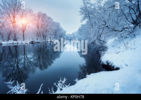 Winter Wald am Fluss bei Sonnenuntergang. Bunte Landschaft mit schneebedeckten Bäumen, zugefrorenen Fluss mit Reflexion im Wasser. Saisonale. Verschneite Bäume, See, Stockfoto