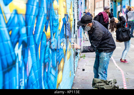 Graffiti street artist tragen eine Beatmungsmaske sprühen die Wände in Fleur Street, London, UK Stockfoto