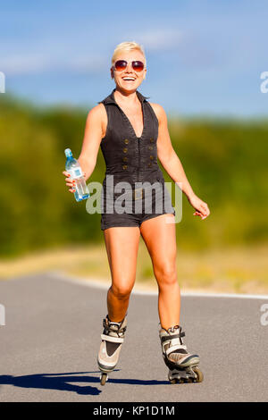 Junge blonde Frau reitet auf Rollen mit Wasser trinken in einer Flasche Stockfoto