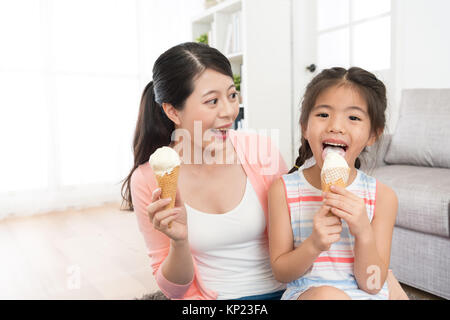 Nettes hübsches kleines Kind Mädchen Gesicht zur Kamera lecken Eis zu Hause und glückliche Mutter an ihre Tochter Gefühl Glück im Sommer. Stockfoto