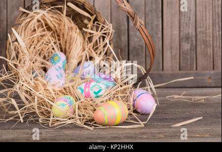 Bunte Ostereier verschüttete aus einem Korb auf einem Holz- Oberfläche Stockfoto