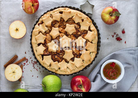 Hausgemachte, traditionelle amerikanische Apfelkuchen mit Stars in eine Auflaufform, rote und grüne Äpfel ganz und geschnitten, zimtstangen und ein Glas eingerichtet. Stockfoto