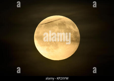 Vollmond/Vollmond scheint in dunkler Nacht, Amber Mond mit einigen wenigen geschwollene, trübe Wolken und ein Flugzeug/ein Flugzeug vorbei, in der Ferne. Stockfoto