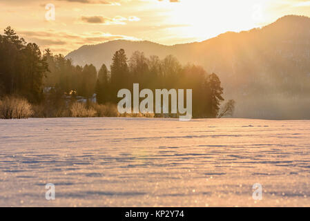 Eine malerische Landschaft mit Bäumen, Bergen und Nebel über einen gefrorenen Schnee See in den Strahlen der Sonne bei Sonnenaufgang Stockfoto