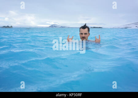 Der bärtige Mann mit lustigen Frisur entspannen im geothermischen Pool auf dem Hintergrund der Schnee Berge und bewölkter Himmel im Freien in Island. Er schaut in Stockfoto