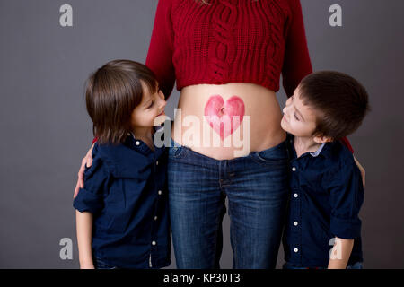 Schöne Kinder im Vorschulalter, Brüder, umarmt ihre schwangere Mutter, freudig erwartet großen Brüder zu sein. Rote Heide auf Mütter Bauch gezogen, küssen Stockfoto