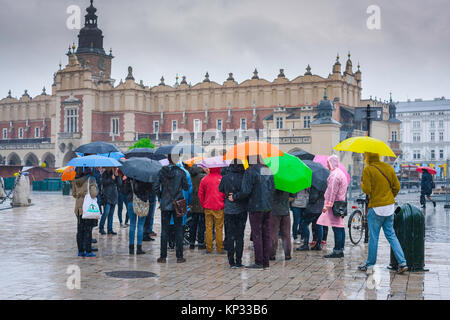 Touristen regen Schirme Europa, unter Sonnenschirmen im schweren Regen eine Reisegruppe lauschen ihren Führer im großen Marktplatz in Krakau, Polen. Stockfoto